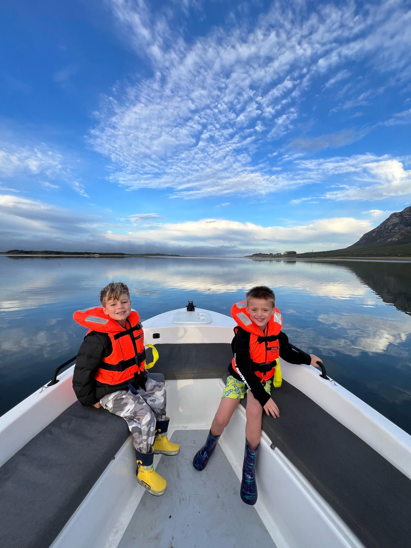 Two boys in life jackets on a boat at sunrise on the glassy Hermanus lagoon