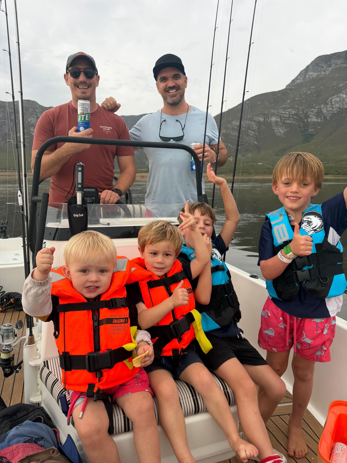 Dads and children giving thumbs up on the boat with the mountain behind