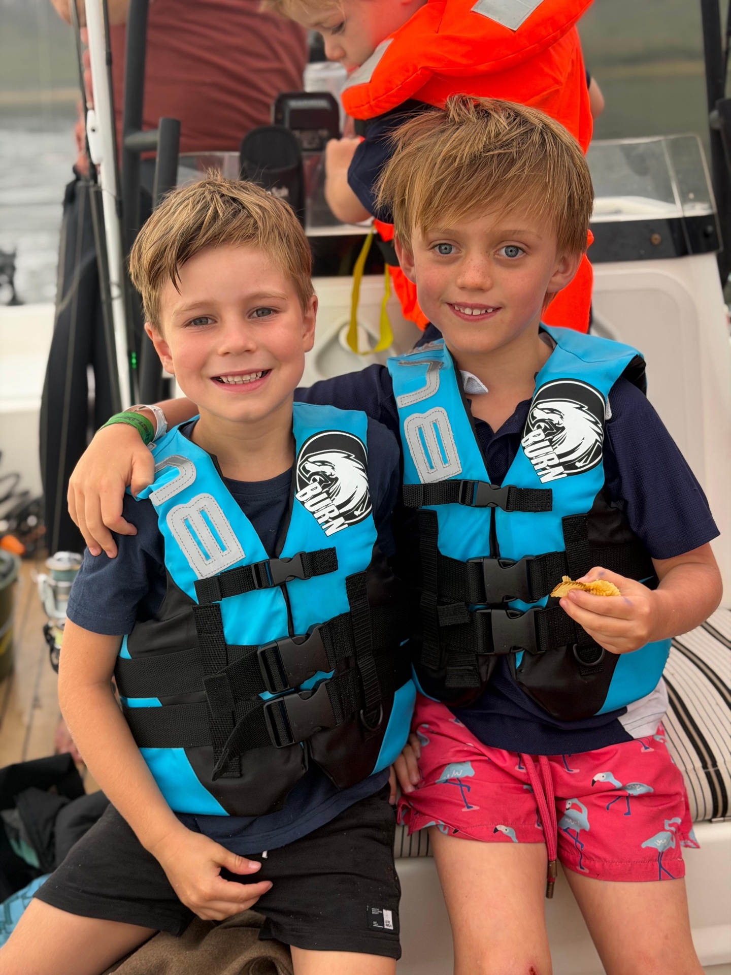 Two brothers in life jackets sitting together on the boat